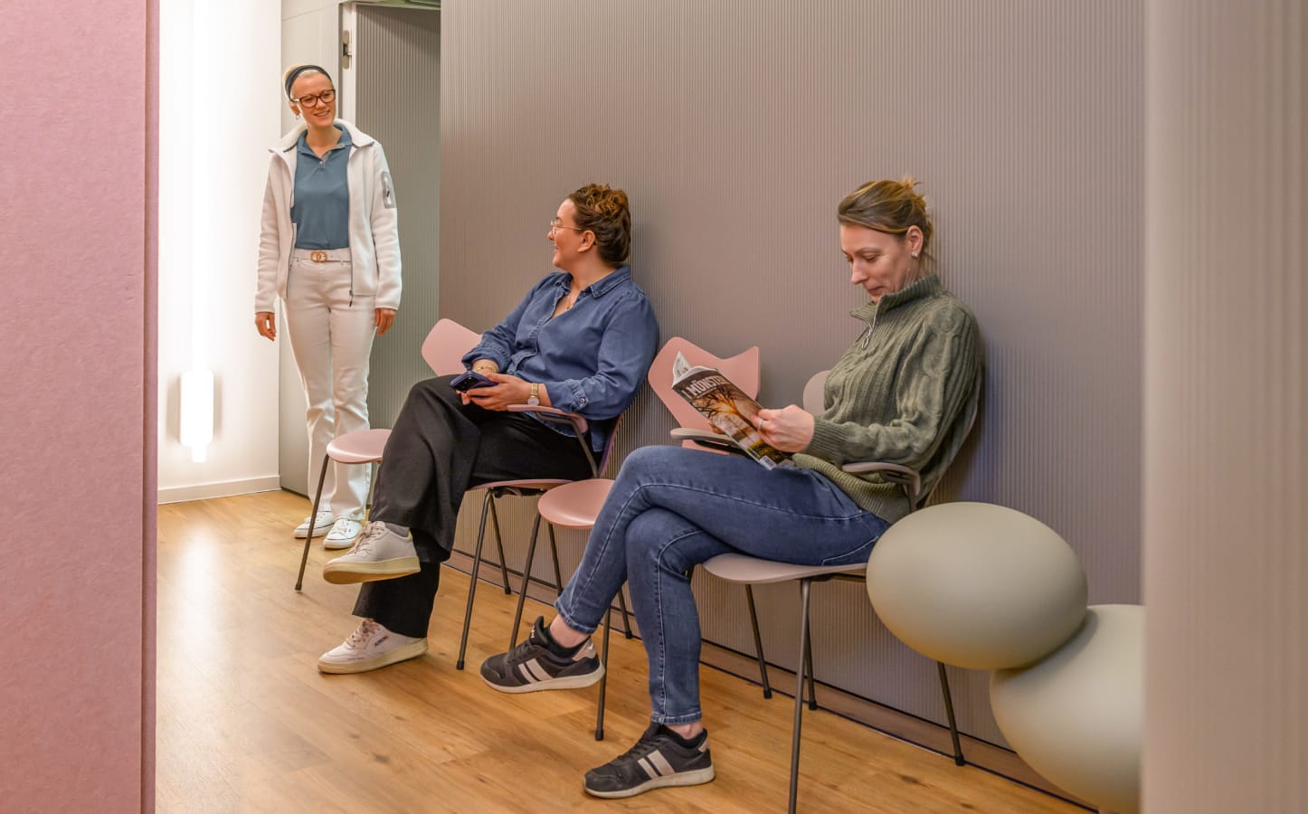 Zwei Patientinnen sitzen im Wartebereich der neuen, modernen Praxisräumlichkeiten und werden von einer Mitarbeiterin aufgerufen